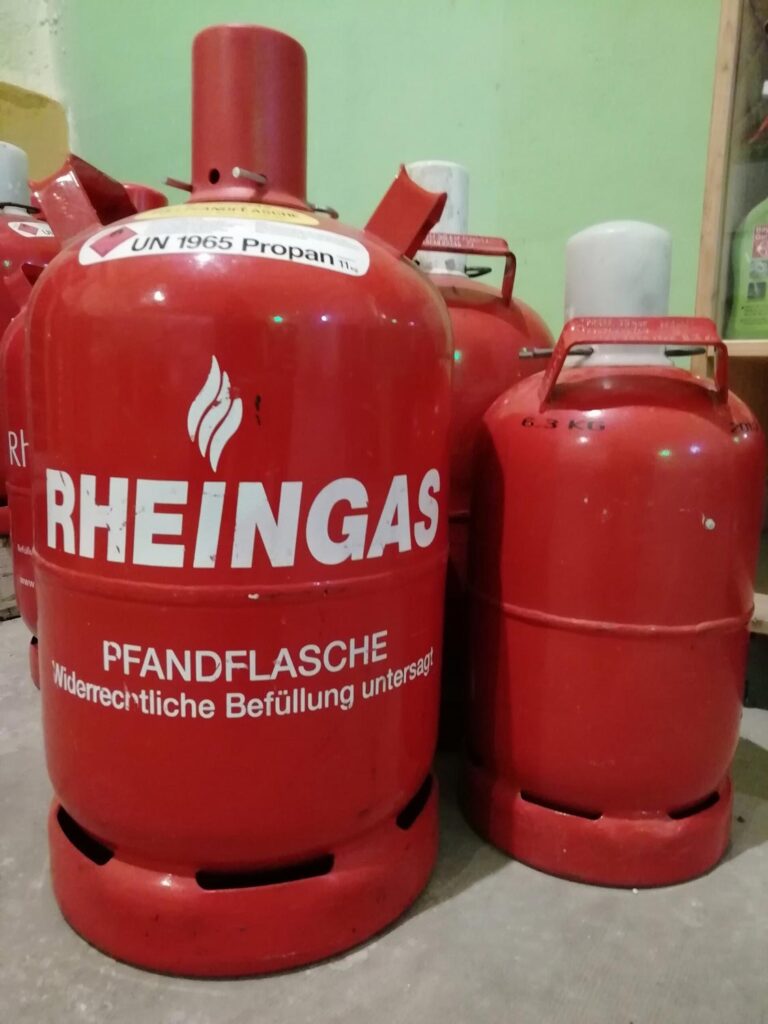 Zwei rote Propangasflaschen mit weißer Aufschrift stehen nebeneinander im Raum