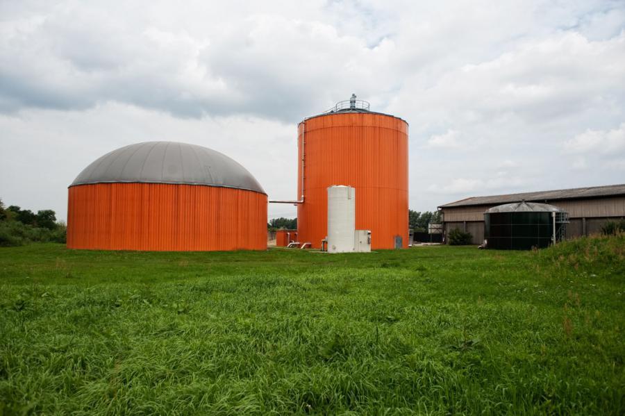 Zwei leuchtend orangefarbene Silos stehen auf einer Wiese unter bewölktem Himmel